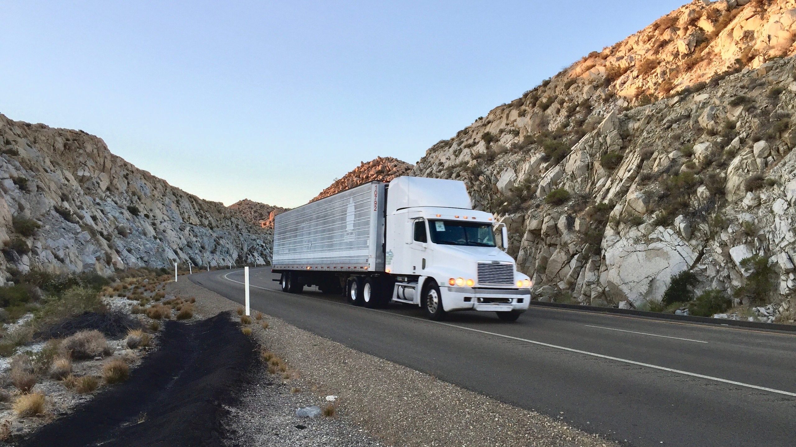 White semi-truck hauling a trailer on a desert road, showcasing efficient partial truckload shipping in a rugged landscape