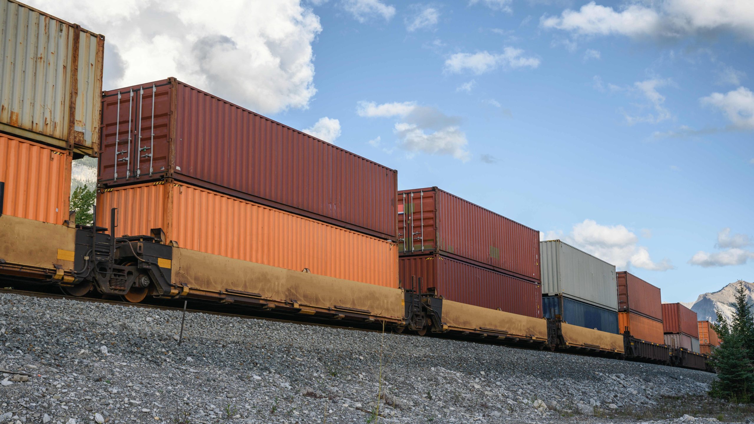 Intermodal shipping containers stacked on a train, showcasing seamless, efficient freight transport through rail with a clear sky in the background.