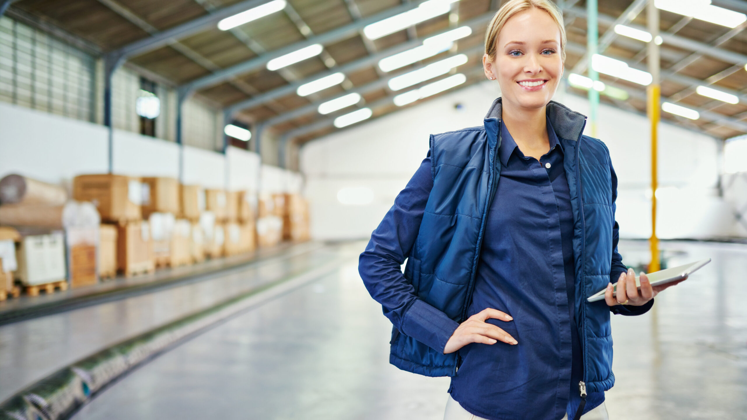 Smiling warehouse manager using a digital device in a well-organized warehouse, showcasing the efficiency of a 3PL logistics company.