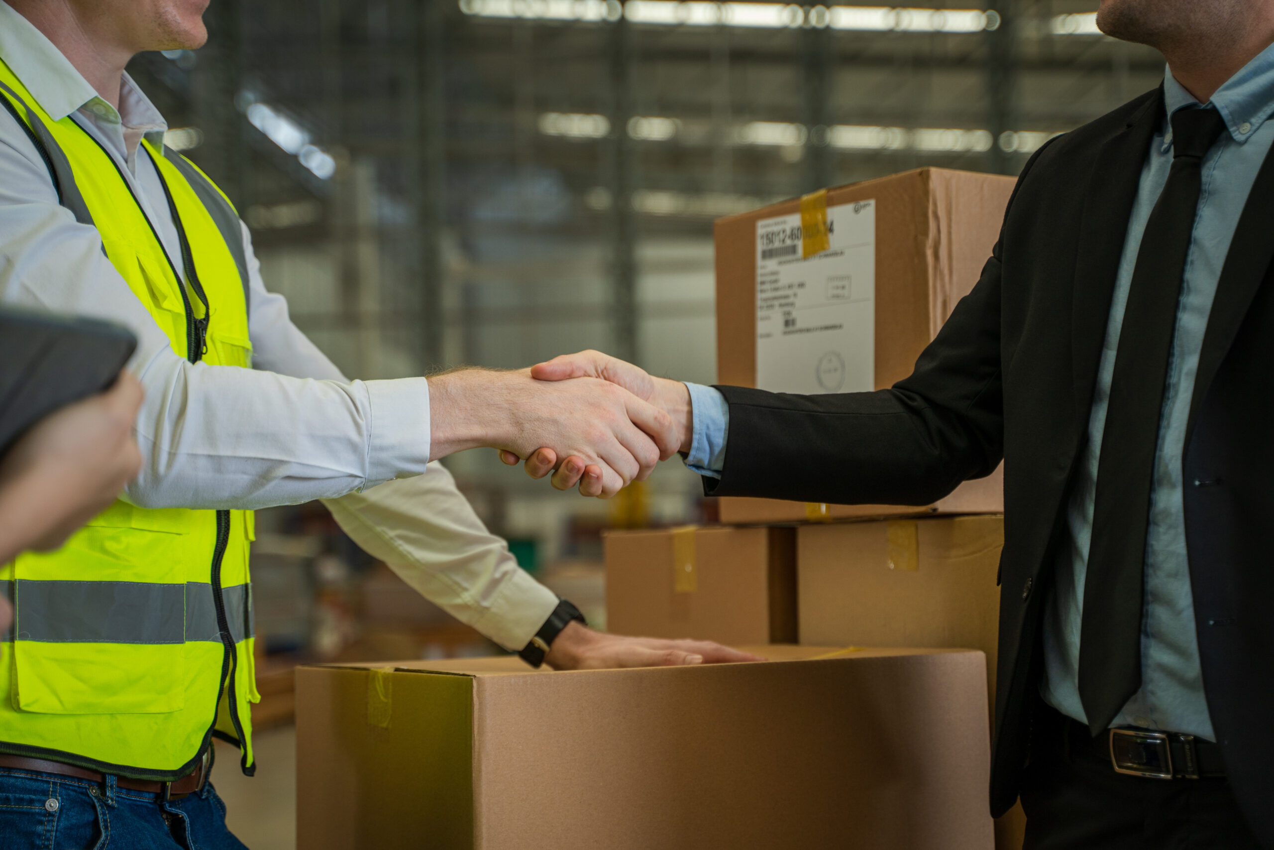 Warehouse manager shaking hands with a business partner in a large warehouse, symbolizing a successful 3PL logistics partnership.