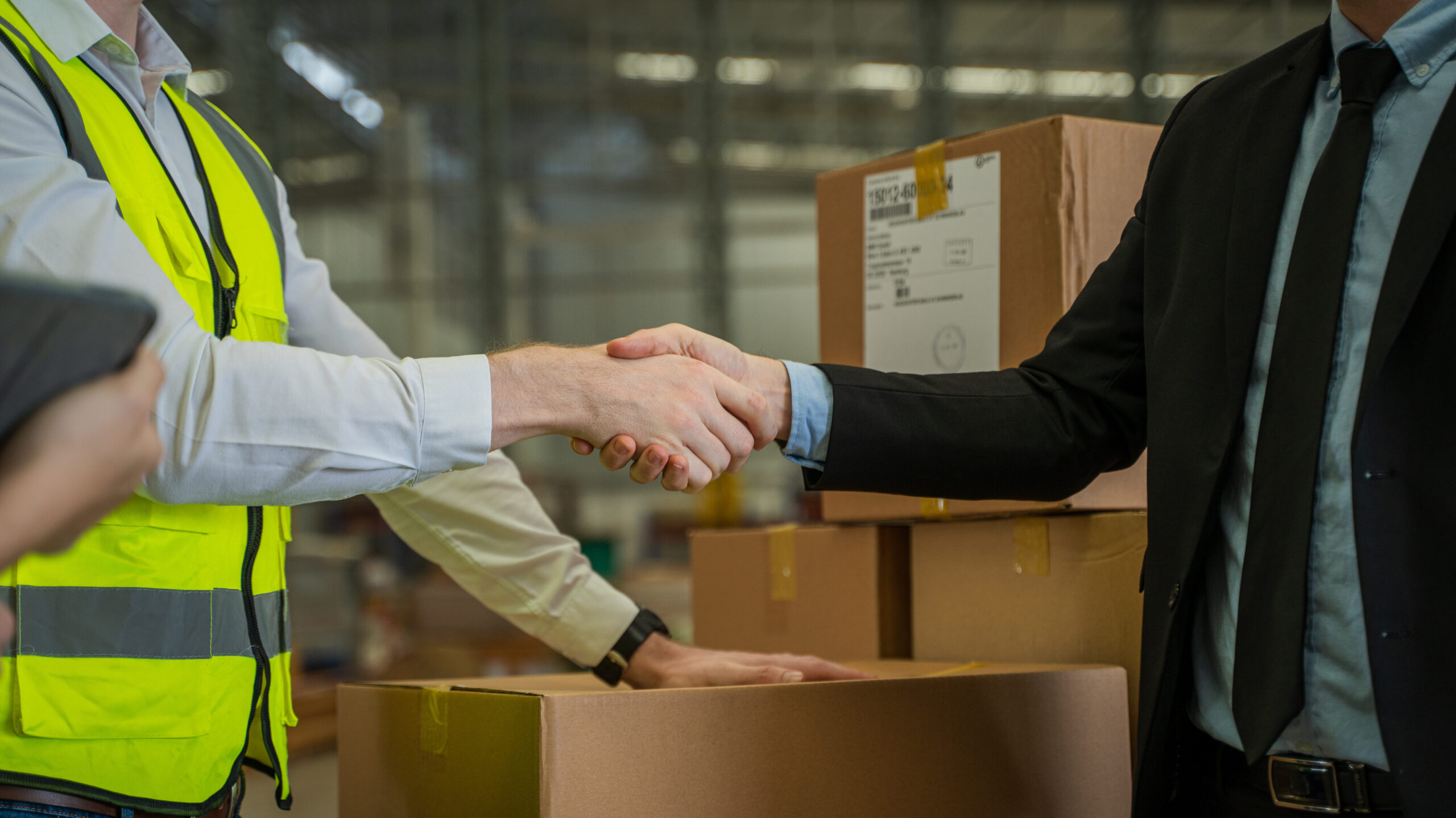 Warehouse manager shaking hands with a business partner in a large warehouse, symbolizing a successful 3PL logistics partnership.