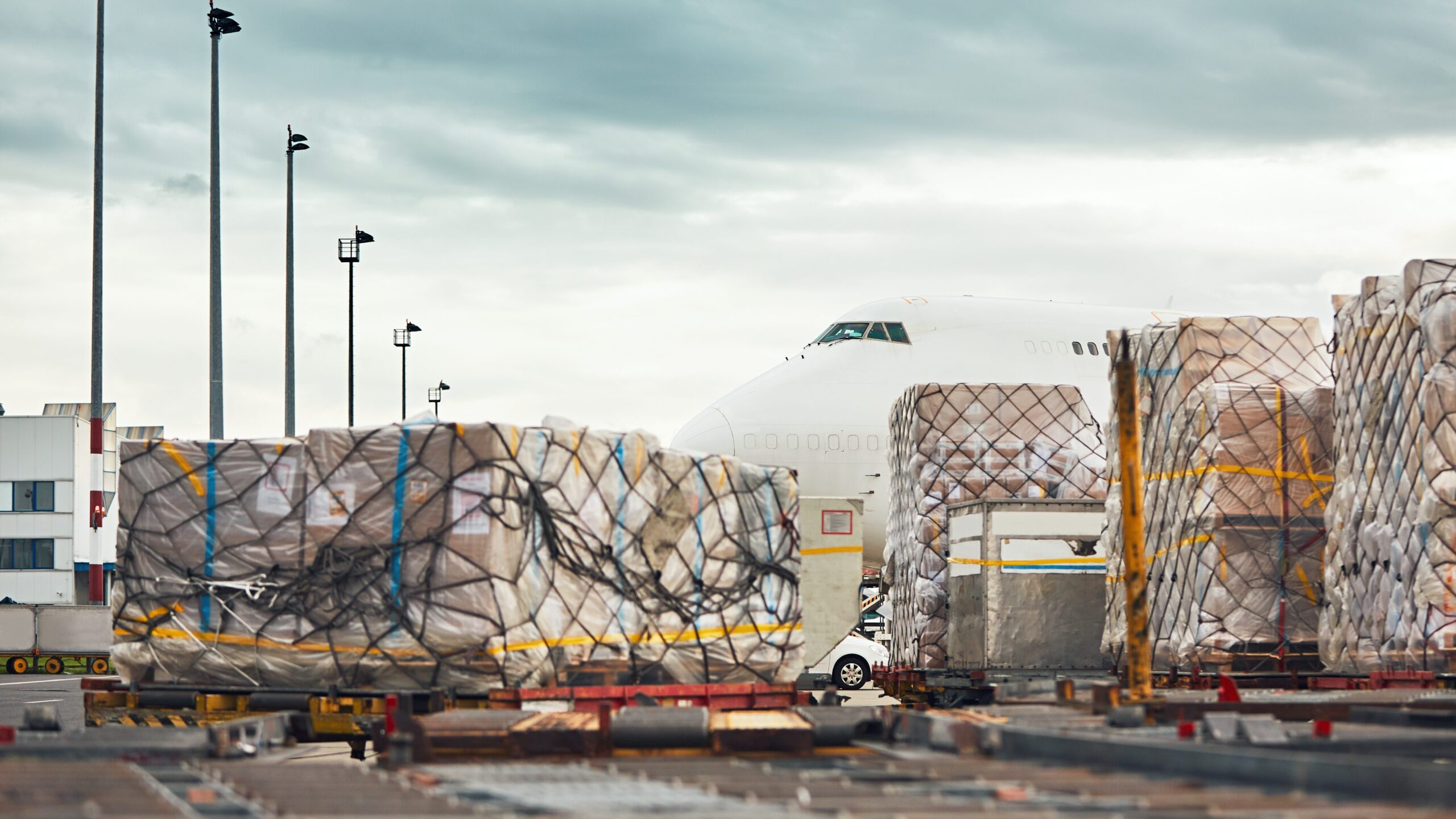 Cross Border Logistics: Cargo being loaded onto an airplane for international shipping, showing freight pallets wrapped and ready for transport at an airport.