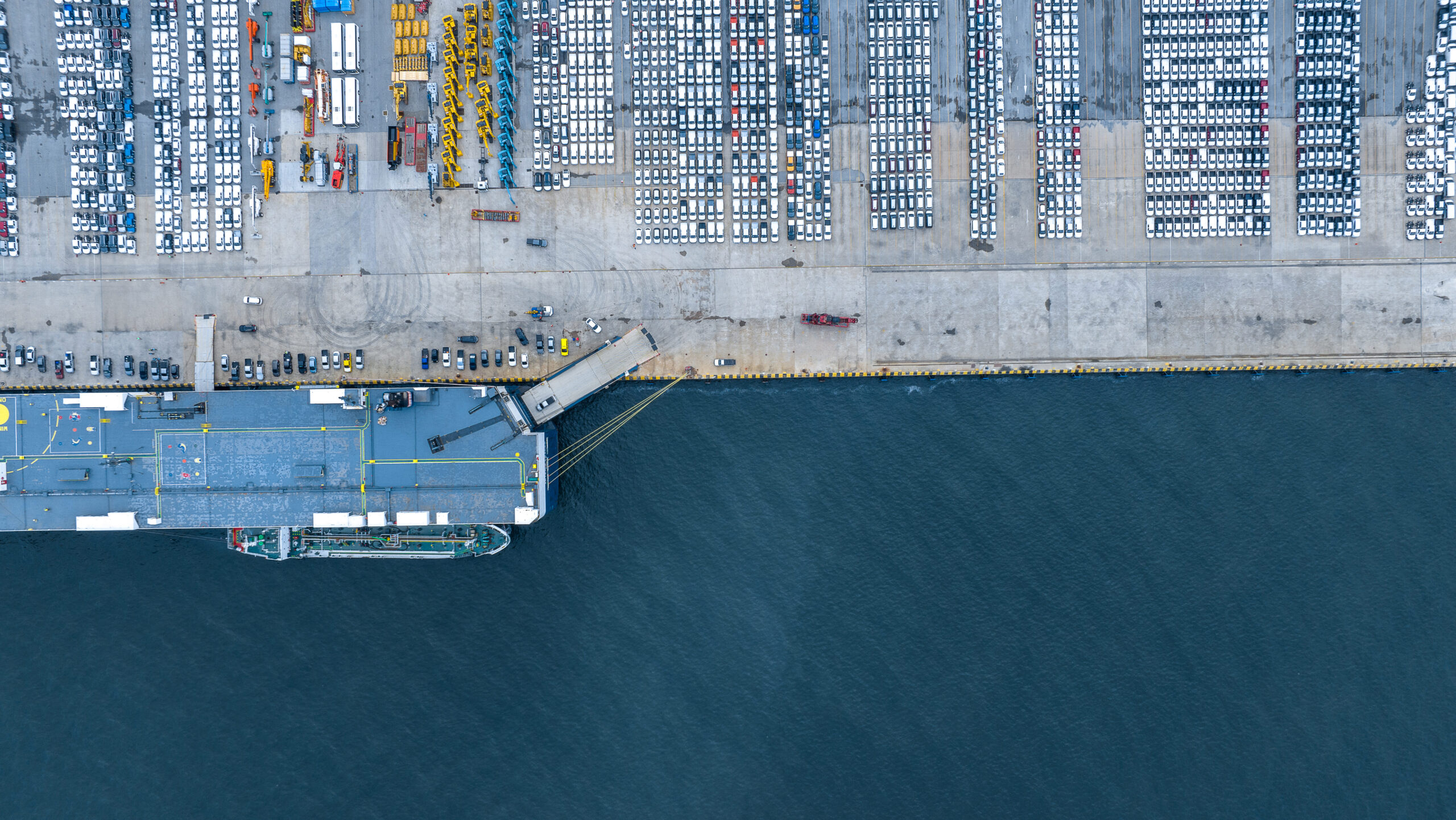 Aerial view of a roll-on/roll-off cargo ship docked at a port with rows of new cars ready for export or import.