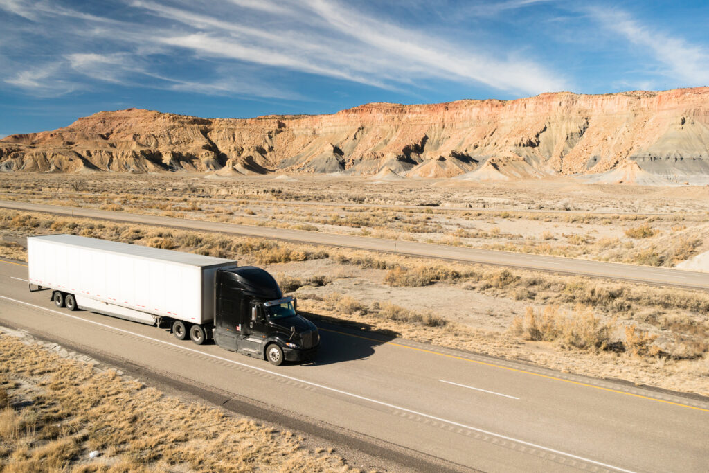 Black semi-truck providing temperature-controlled LTL shipping services, traveling through a desert landscape with mountains in the background.