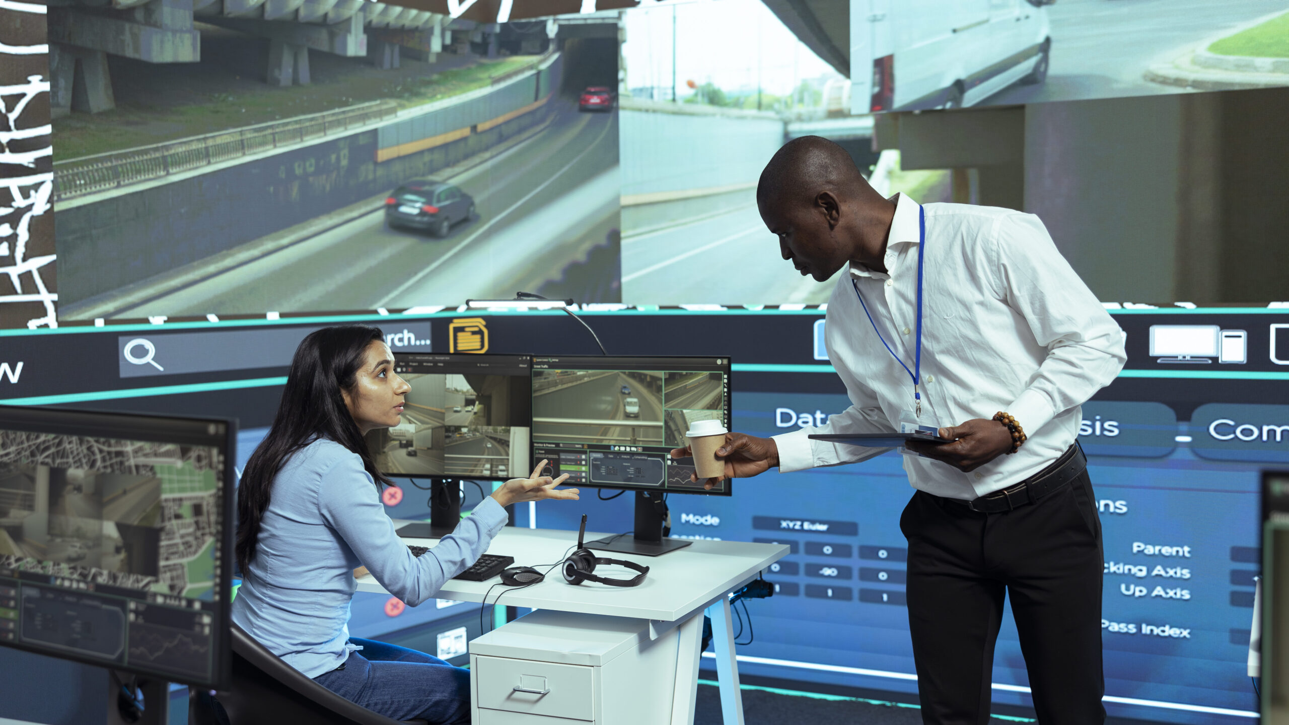 Team discussing logistics technology solutions with live data monitoring and traffic analysis displays in a control room setting.