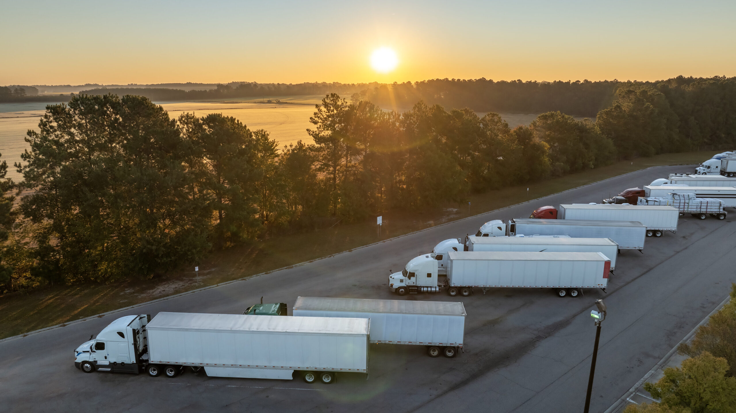 Freight trucks parked at a rest area near a scenic highway during sunrise, symbolizing the demand and activity in the U.S. freight industry.